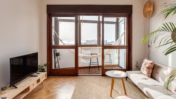 Een moderne woonkamer met een grote schuifpui naar een balkon, een flatscreen televisie, een bank en een kleine ronde tafel.