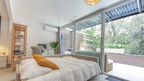 A modern bedroom with a large bed, a wooden side table, a chair, and a view of the outdoors through large glass doors. - King-size bed with terrace and Air Conditioning!
 (Las Condes)