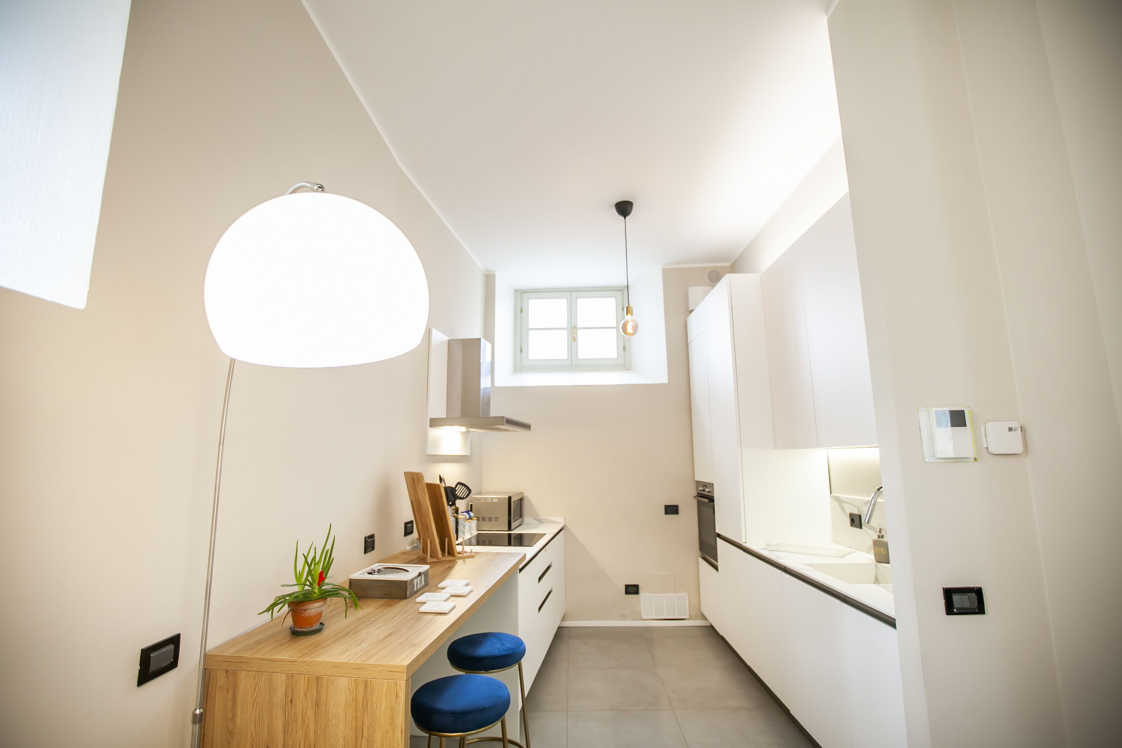Uma cozinha moderna com bancada de madeira, dois banquetes azuis, luminária pendente e janela que ilumina naturalmente o espaço.