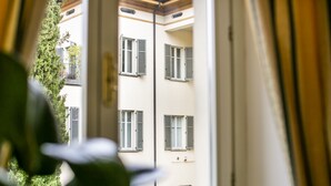 A view through a window with a plant in the foreground, revealing a building with multiple windows and balconies.