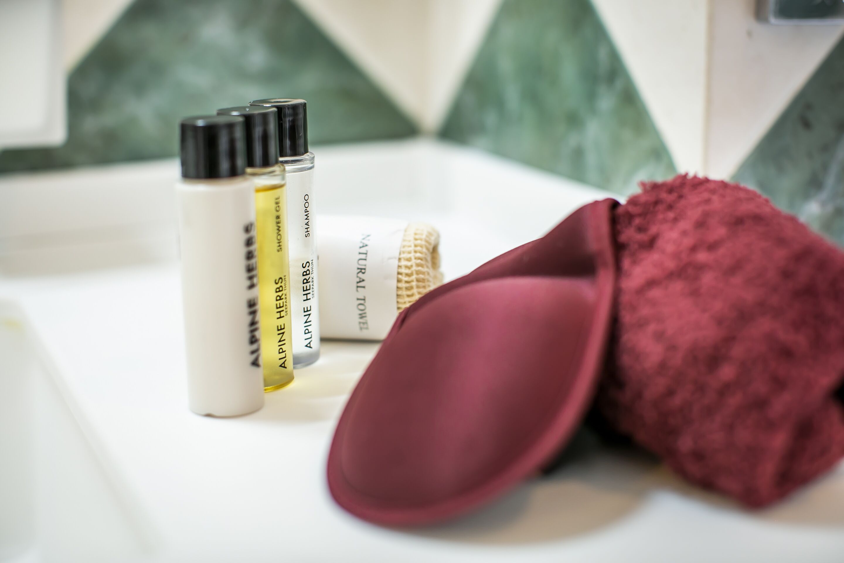 A bathroom with a white sink, a red towel, and three bottles of shower gel.