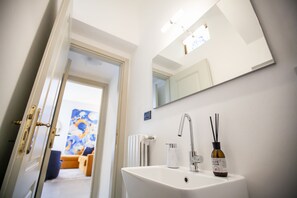 Un baño con un lavamanos blanco, un espejo y una botella de aceite de oliva.