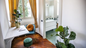 A room with a desk, a chair, a potted plant, and a view of a bathroom through an open door.