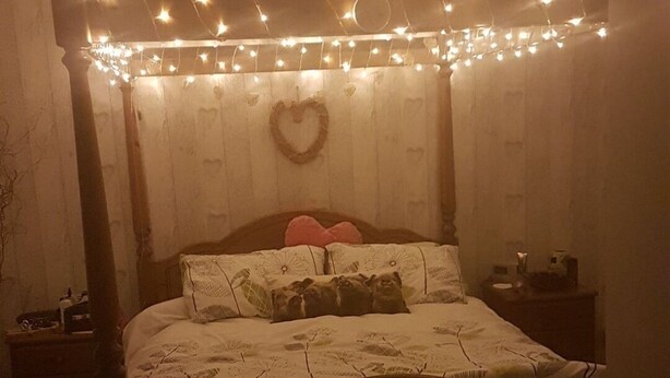 Une chambre à coucher faiblement éclairée, avec un lit en bois, des décorations en forme de cœur et des guirlandes lumineuses.