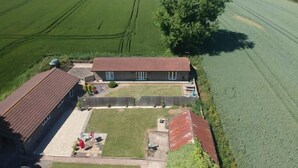 Vue aérienne d’une propriété comprenant un grand champ, une maison avec un toit rouge et une cour clôturée.