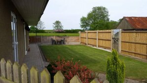 Un jardin avec une clôture en bois, une petite pelouse et un espace patio aménagé avec du mobilier d’extérieur.
