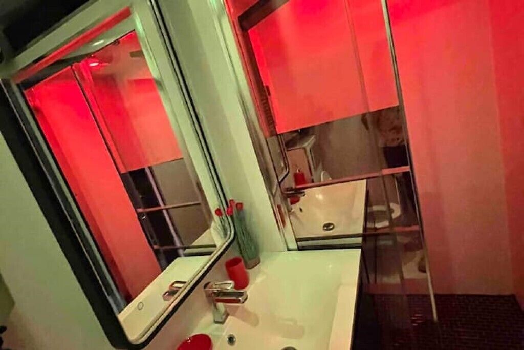 A bathroom with a white sink, a mirror, and red lighting.