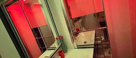 A bathroom with a white sink, a mirror, and red lighting.