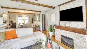 Un salón espacioso con un sofá blanco, una chimenea y un televisor instalado en una pared de ladrillo.