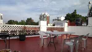 Terraza en la azotea con una mesa, sillas, una parrilla y dos cubos de comida.