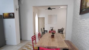 Un comedor con una larga mesa de madera, sillas rojas y amarillas, y una planta en maceta.
