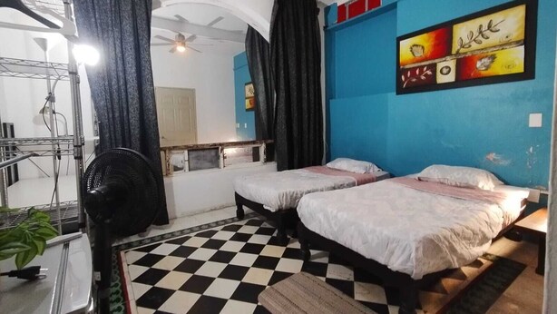 Una habitación con dos camas, suelo a cuadros, ventilador de techo y un cuadro en la pared.