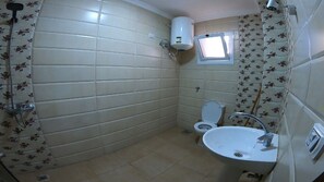 Compact bathroom with a toilet, sink, and shower, featuring a floral tile pattern and a wall-mounted heater.