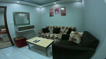 A living room with a sofa, a coffee table, a TV, and a small red stool.
