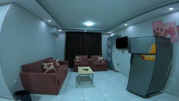 A living room with a sofa set, a coffee table, a refrigerator, and a TV mounted on the wall.