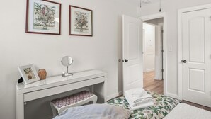 A bedroom with a white dresser, a bed with floral bedding, a ceiling fan, and two framed botanical prints on the wall. - Cozy Cottage, Deck + Yard, Near Downtown & 10 min to Parris Island (Beaufort)