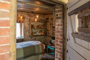 A rustic room with exposed brick walls, a wooden ceiling, and a bed with a checkered bedspread. There are hanging light fixtures and a small table with a chair. - THE PIG at Combe - Devon (Honiton)