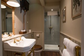 A bathroom with a white sink, gold fixtures, a wooden toilet, a shower with patterned tiles, and a towel rack. - THE PIG at Combe - Devon (Honiton)