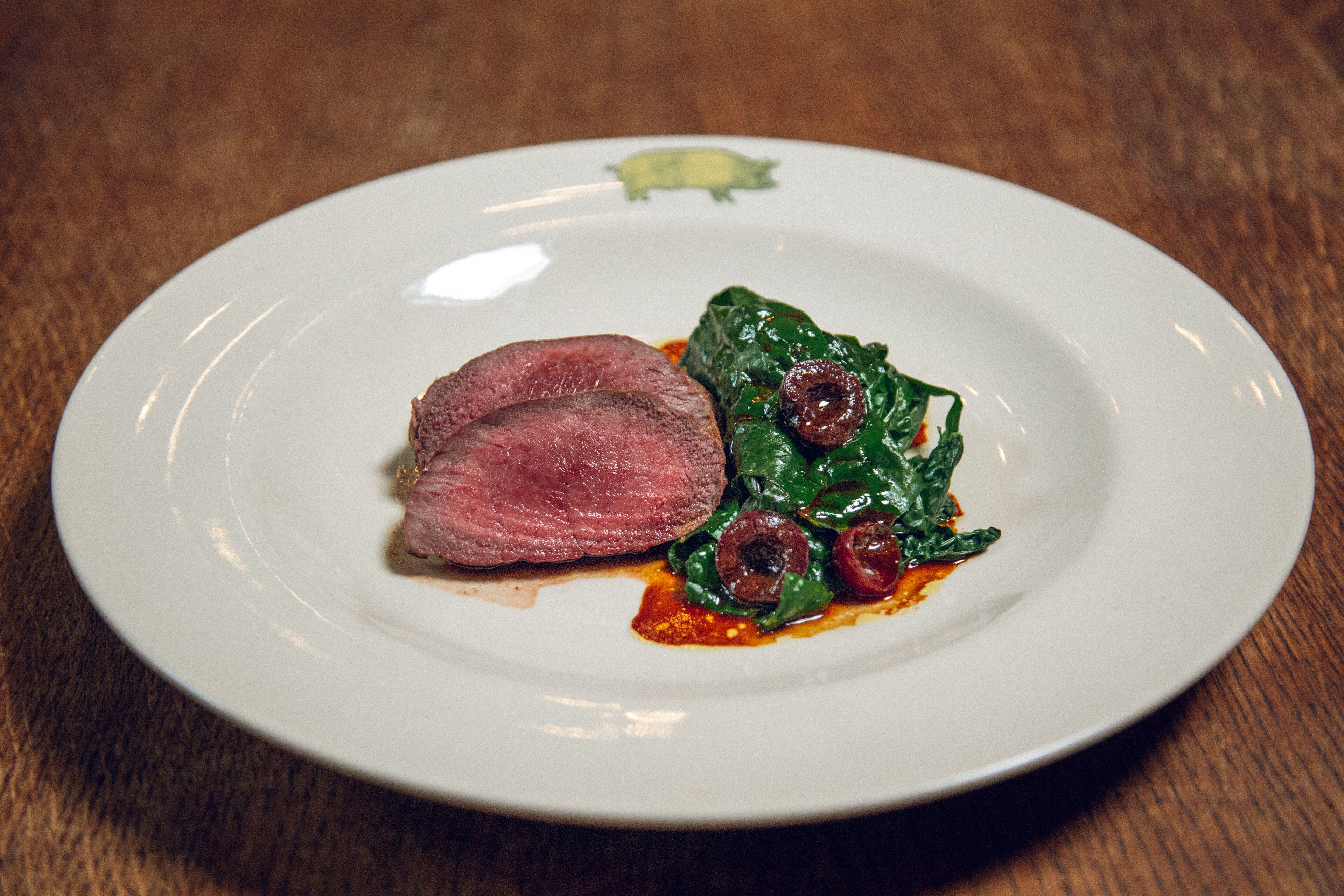 A plate with a slice of meat and greens on a white plate.