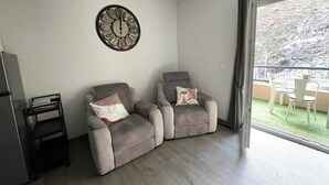 Ein Wohnzimmer mit zwei grauen Sesseln, einem kleinen Tisch und einer Wanduhr.