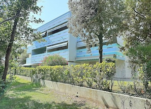 A multi-story building with balconies, surrounded by greenery and a concrete barrier. - Delightful Seaside Flat With ac - Beahost (San Michele al Tagliamento)