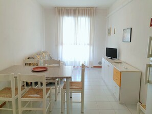 A small, bright room with a dining table, chairs, a sofa, a TV, and a cabinet. - Delightful Seaside Flat With ac - Beahost (San Michele al Tagliamento)