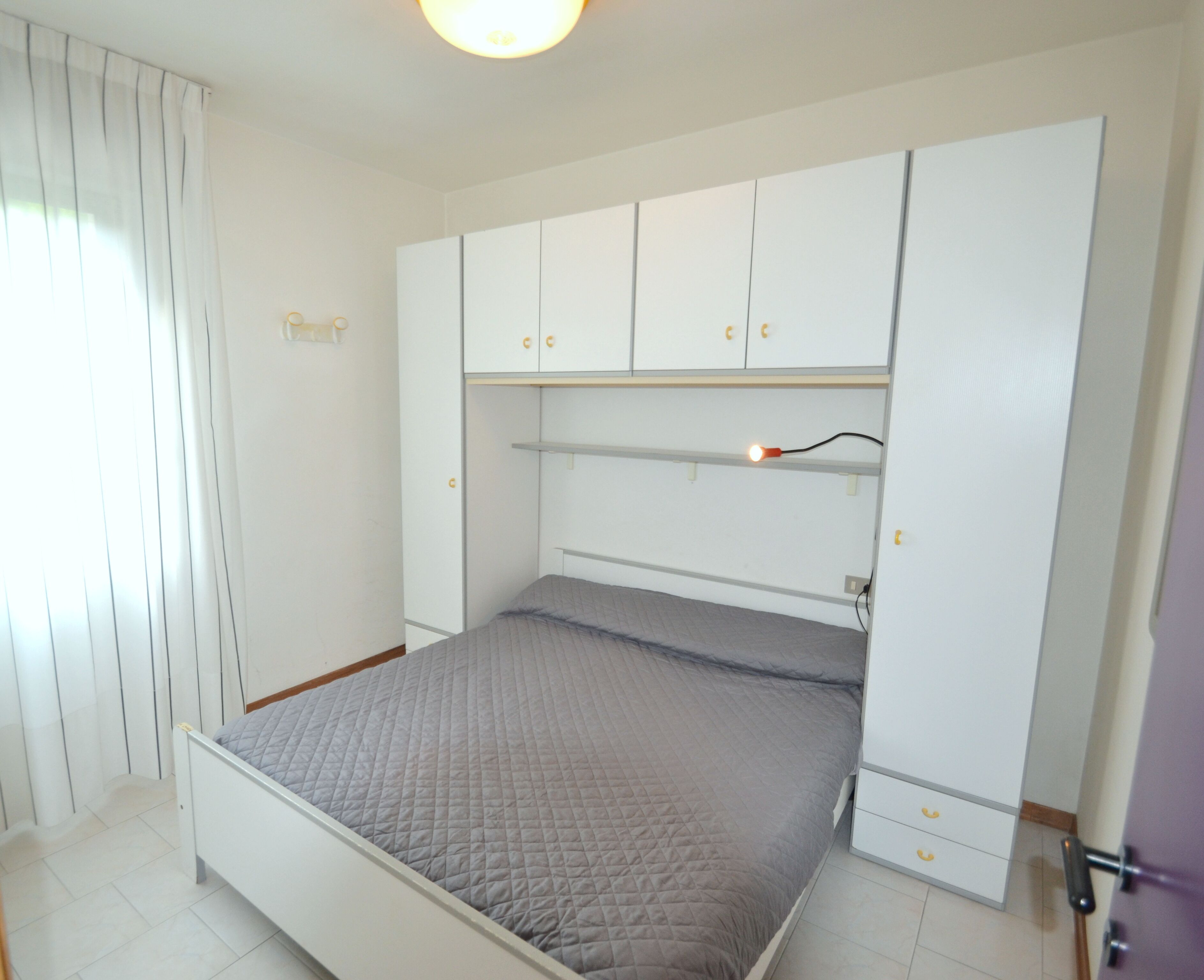 A bedroom with a bed, white wardrobe, and a ceiling light.