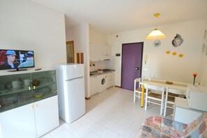 Une cuisine compacte équipée d’un réfrigérateur, d’un lave-linge et d’un coin repas avec une table et des chaises.