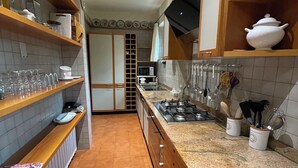 A kitchen with wooden shelves, a stove, and various kitchen utensils. - 3 minutes from the lake, with a large terrace and garden (Leggiuno)