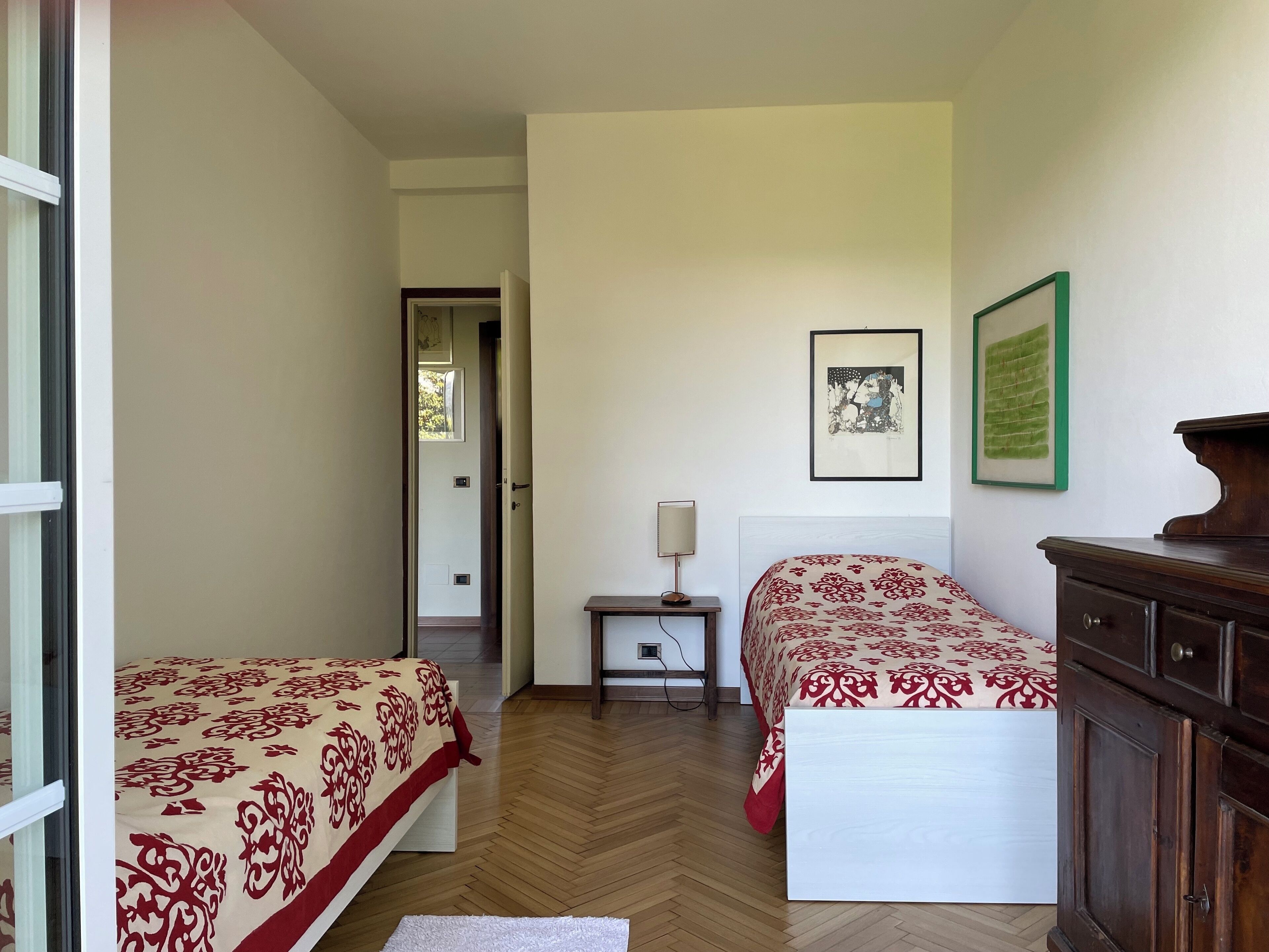 A bedroom with two beds, a nightstand, a dresser, and a door leading to another room.