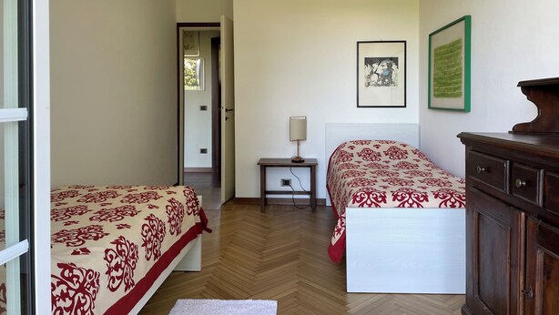 A bedroom with two beds, a nightstand, a dresser, and a door leading to another room. - 3 minutes from the lake, with a large terrace and garden (Leggiuno)