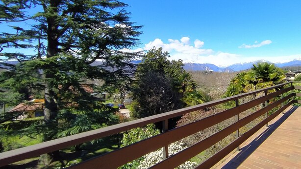 A wooden deck with a view of a mountainous landscape, including snow-capped peaks and dense greenery. - 3 minutes from the lake, with a large terrace and garden (Leggiuno)