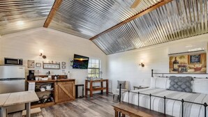 A cozy, well-lit room with a wooden table, a sofa, and a kitchen area with a microwave and cabinets. - Wine Country Cottage With Scenic Hill Country Views (Harper)