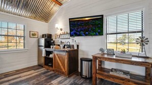 A kitchen with a wooden ceiling, a large TV, a windmill decoration, and a rustic wooden table. - Wine Country Cottage With Scenic Hill Country Views (Harper)