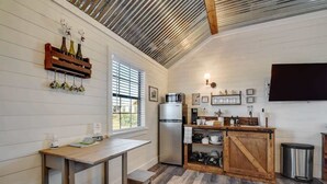 A compact kitchen with a wooden island, a refrigerator, and a mounted TV. - Wine Country Cottage With Scenic Hill Country Views (Harper)