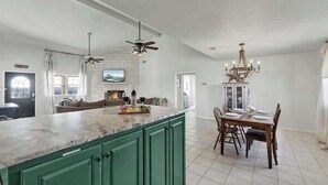 A spacious kitchen with green cabinets, a marble countertop, and a dining area with a chandelier.