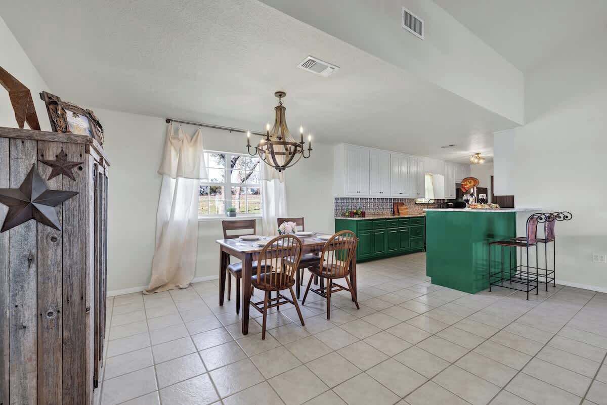A spacious kitchen with white cabinets, a green island, and a dining area with a table and chairs.