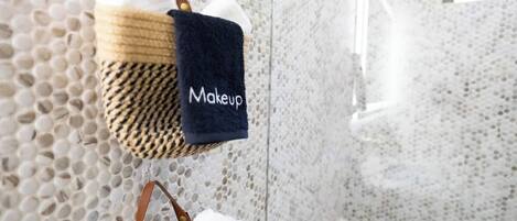 A bathroom with a textured wall and a towel rack holding a black towel labeled "Makeup."