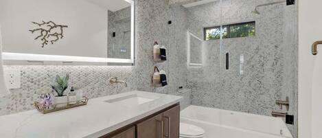 A modern bathroom with a large mirror, two sinks, a toilet, and a bathtub.