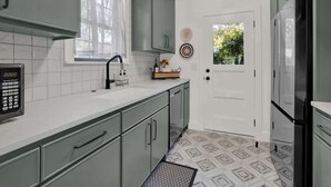 A kitchen with a white countertop, green cabinets, a black microwave, and a refrigerator.