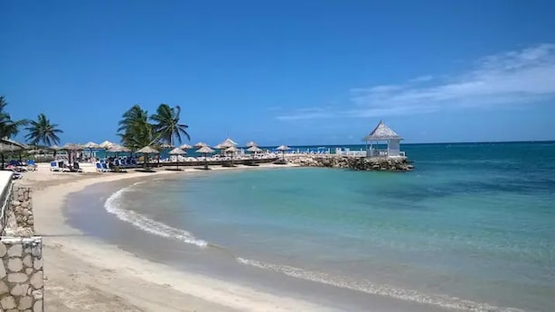 A beach with a pier, palm trees, and beach umbrellas. - Apt - Gated Community-sleeps 4-balcony-parking (Runaway Bay)