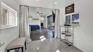 A modern hotel room with a large mirror, a bed, a small seating area, a ceiling fan, and a view of the outdoors. - K Loma Vista With Hill Country Views (Center Point)