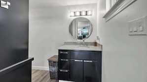 A modern bathroom with a black vanity, a round mirror, and a lighted vanity area. - K Loma Vista With Hill Country Views (Center Point)