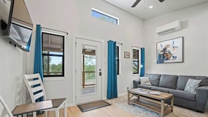 A living room with a sofa, a coffee table, a chair, a door, and a window. - Mimosa Waterfront With Hot Tub (Fredericksburg)