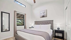 A bedroom with a large bed, a window, a bedside table, and a nightstand. - Mimosa Waterfront With Hot Tub (Fredericksburg)