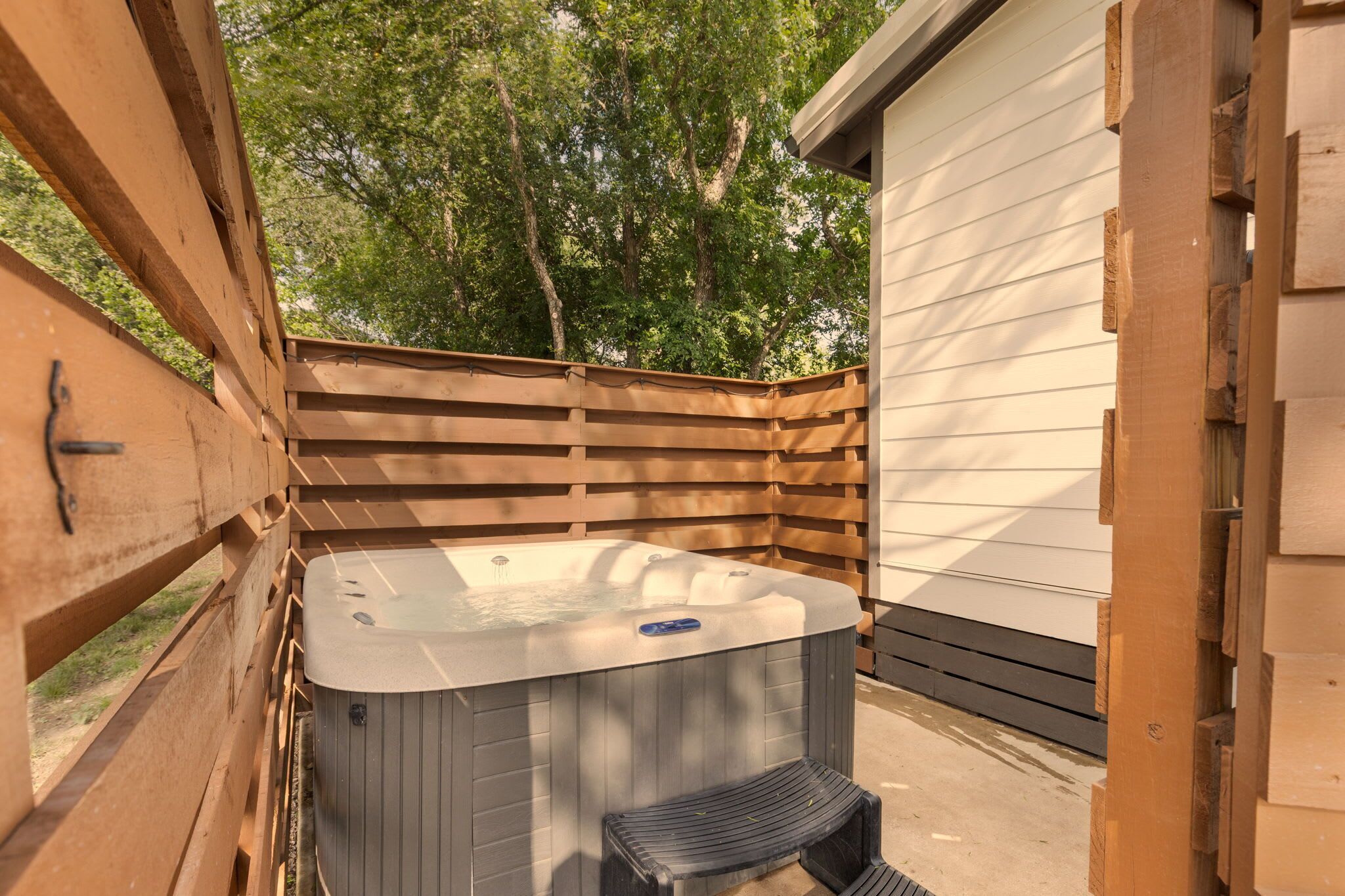 A hot tub in an outdoor wooden deck area with a wooden fence and a building in the background.