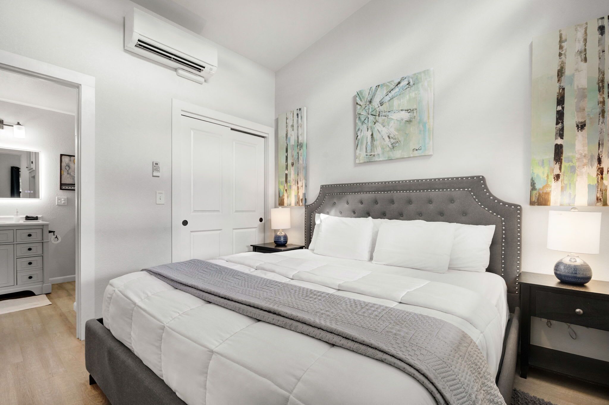 A bedroom with a bed, bedside tables, a dresser, and artwork on the walls.