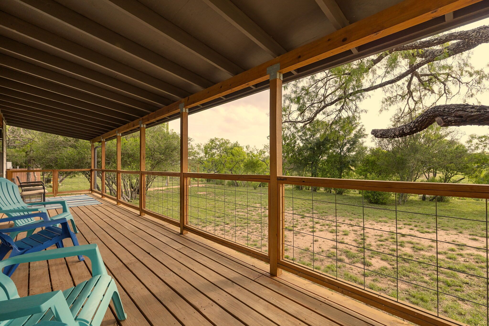 Un espace extérieur abrité, doté d’un plancher en bois et de rampes en métal, offrant une vue sur un paysage verdoyant et des arbres.