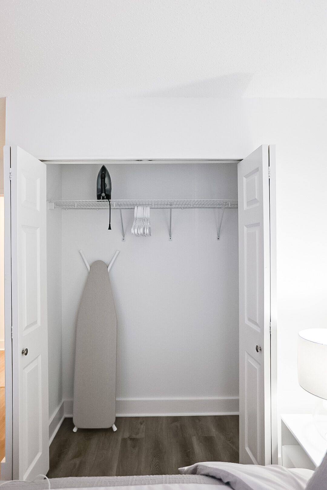 Un petit placard blanc, équipé d’une tringle à vêtements, d’une planche à repasser et d’une étagère située au-dessus.