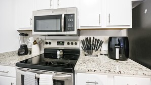 Une cuisine moderne avec des meubles blancs, un micro-ondes noir, une cuisinière, une machine à café et un bloc à couteaux.